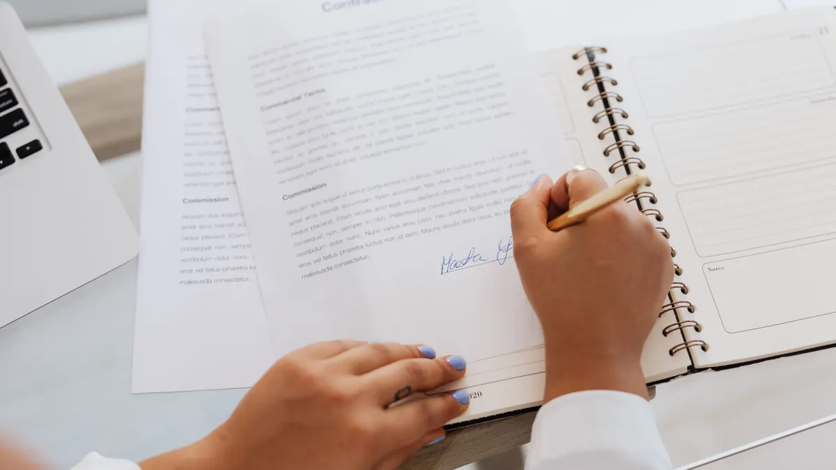 Gros plan de mains signant un contrat sur un bureau avec fournitures de bureau.