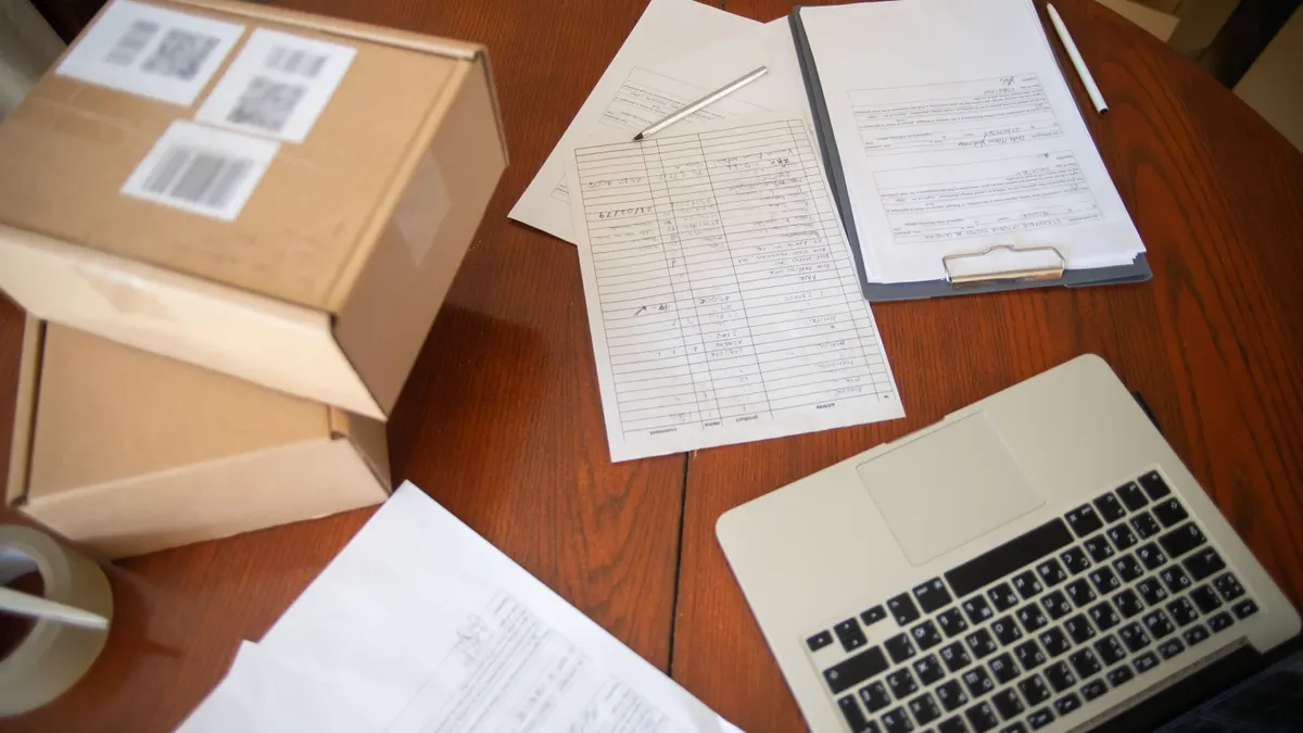 Vue de dessus d'un bureau avec ordinateur portable, documents et cartons pour le commerce en ligne sur table en bois.